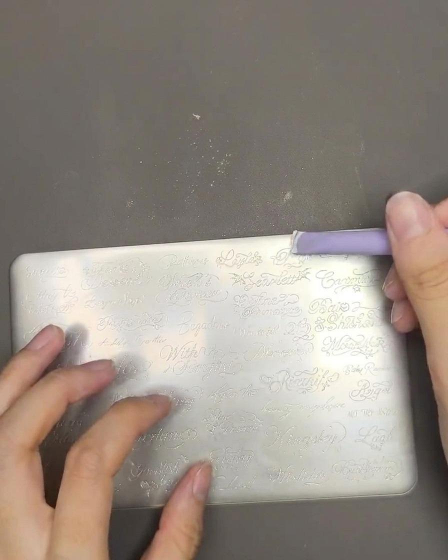 Nahaufnahme von weißem Stamping-Lack, der mit einem violetten Schaber über eine Metall-Stamping-Platte verteilt wird.