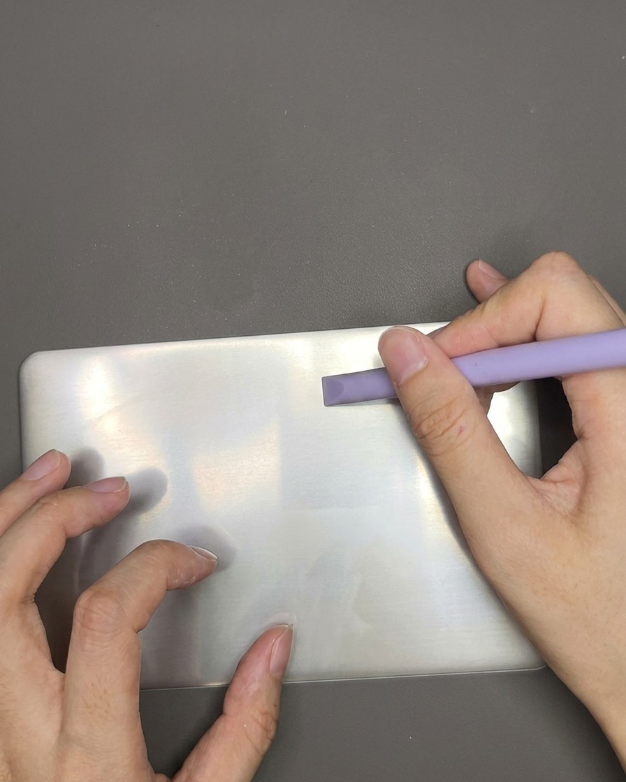Ein Plastikschaber zieht über eine Stamping-Platte, um überschüssigen weißen Lack zu entfernen.