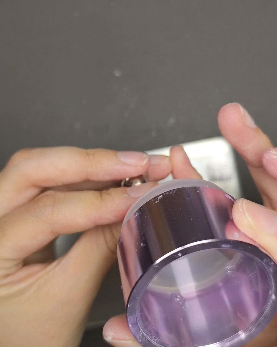 Ein transparenter Stempel wird auf einen roten Cat-Eye-Nagel gedrückt, um den Schriftzug zu übertragen.