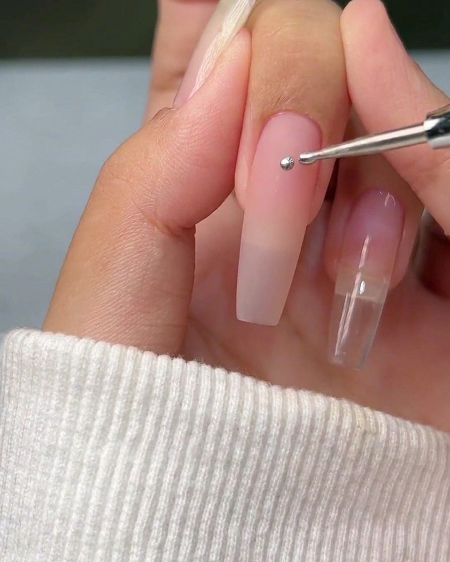 Nahaufnahme eines Dotting-Tools, das einen einzelnen, perfekten Punkt aus silbernem Metallic-Gel auf eine saubere Nageloberfläche setzt.