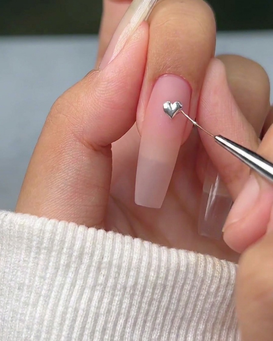 Ein feiner Liner-Pinsel zieht vorsichtig die Kanten eines silbernen Gel-Punktes in eine scharfe, definierte Herzform auf dem Nagel.