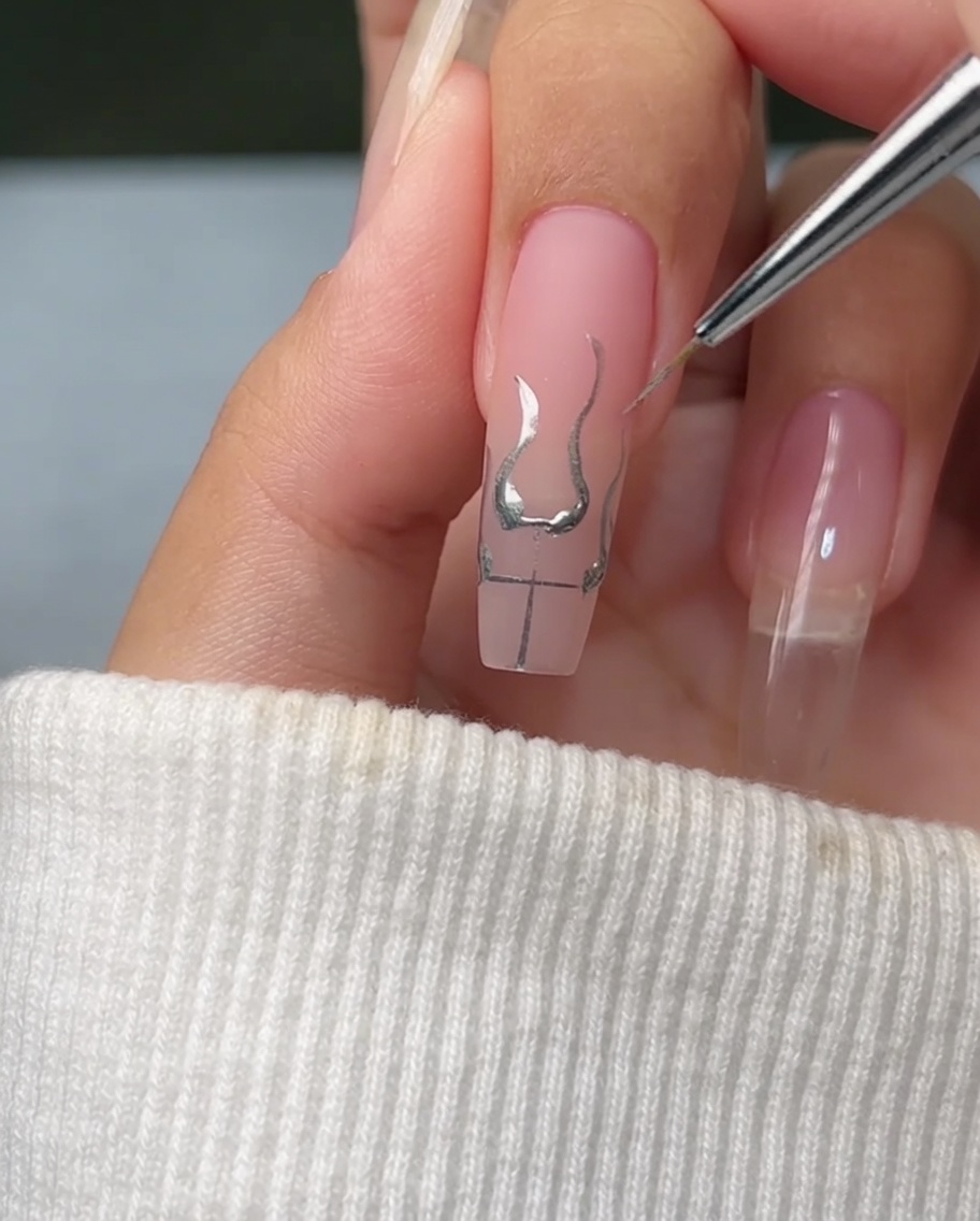 Ein feiner Pinsel füllt die Basis der Flammen-Umrisse auf einem Nagel mit hellem, reflektierendem Metallic-Silber-Gel.
