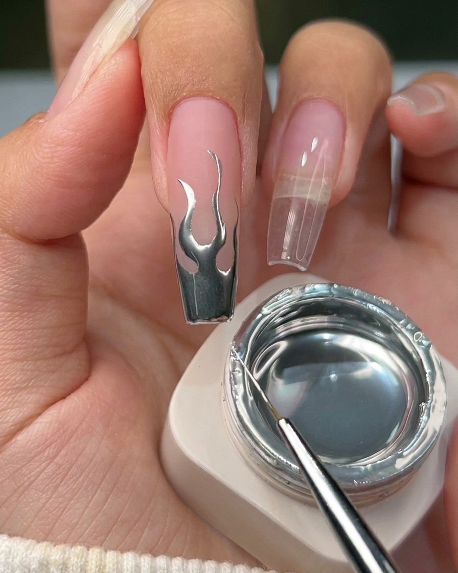 Nahaufnahme eines fertigen Nagels mit einem Metallic-Silber-Flammendesign auf einer neutralen Basis.