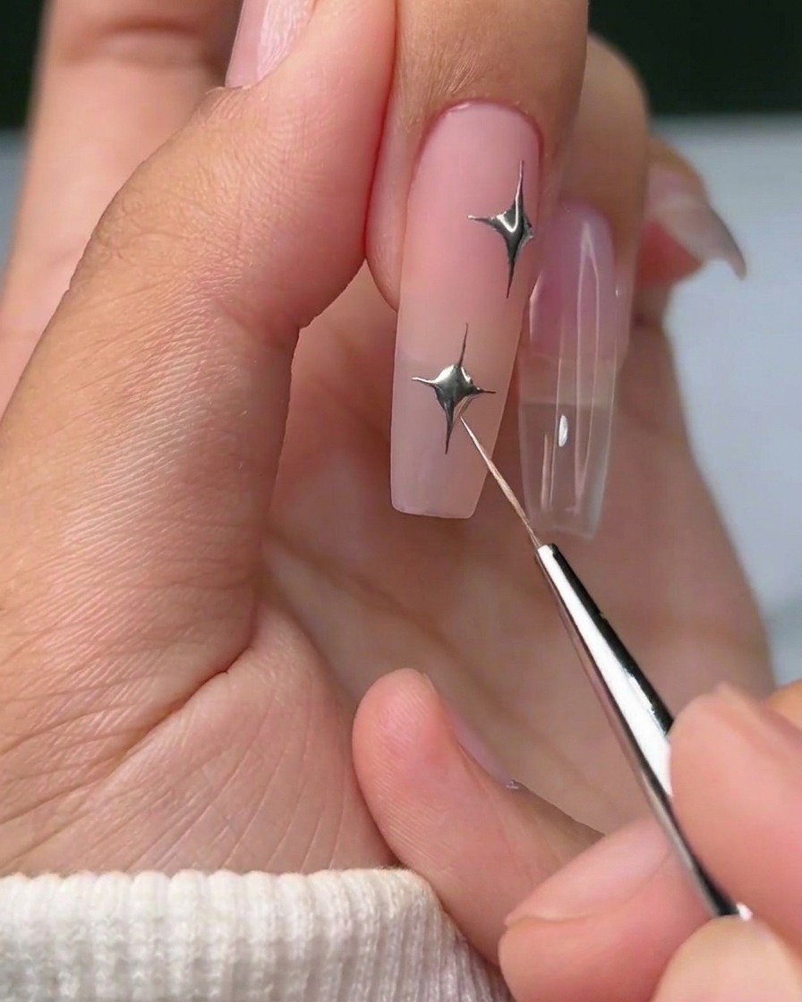 Ein fertiges Nageldesign mit einem metallisch-silbernen vierstrahligen Stern und einem kleinen silbernen Schmuckstein-Akzent.