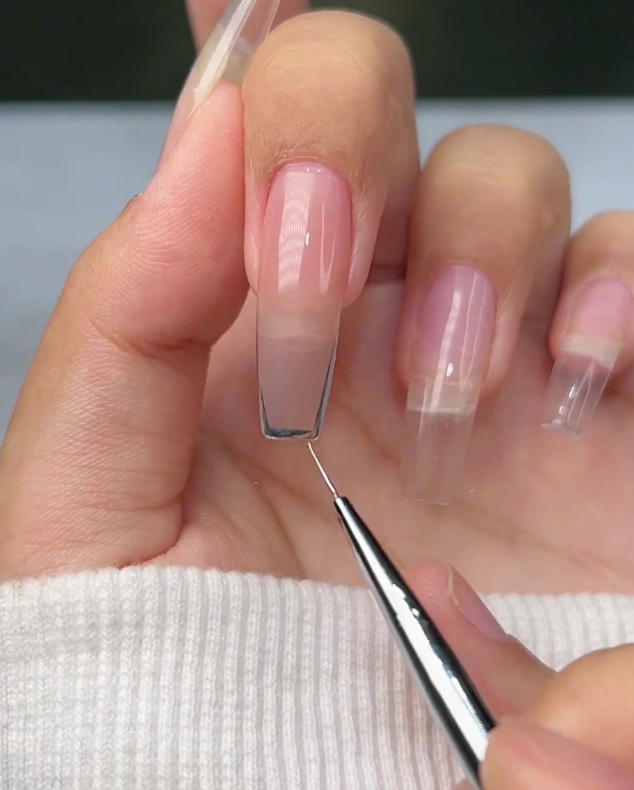 Nahaufnahme eines Liner-Pinsels, der eine geschwungene silberne Umrandung auf der Spitze eines Naturnagels zieht.