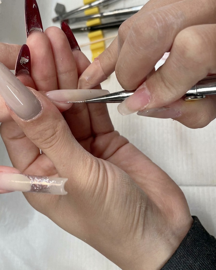 Nahaufnahme eines Liner-Pinsels beim Auftragen von Rosegold-Glitzer auf das Nagelbett.