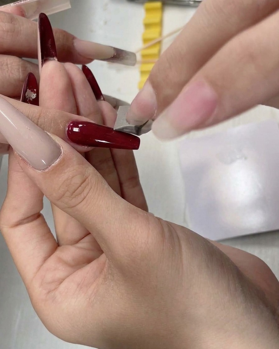 Ein kleines Schwamm-Tool tupft weißes Gel auf den freien Rand eines langen Nagels.