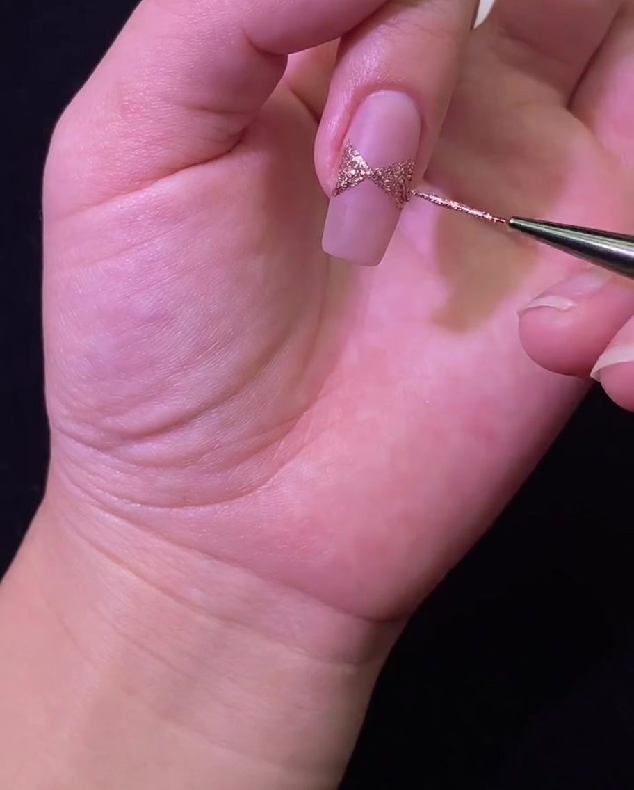Ein Nagel unter einer UV/LED-Lampe zur Härtung des Roségold-Glitzerdesigns.
