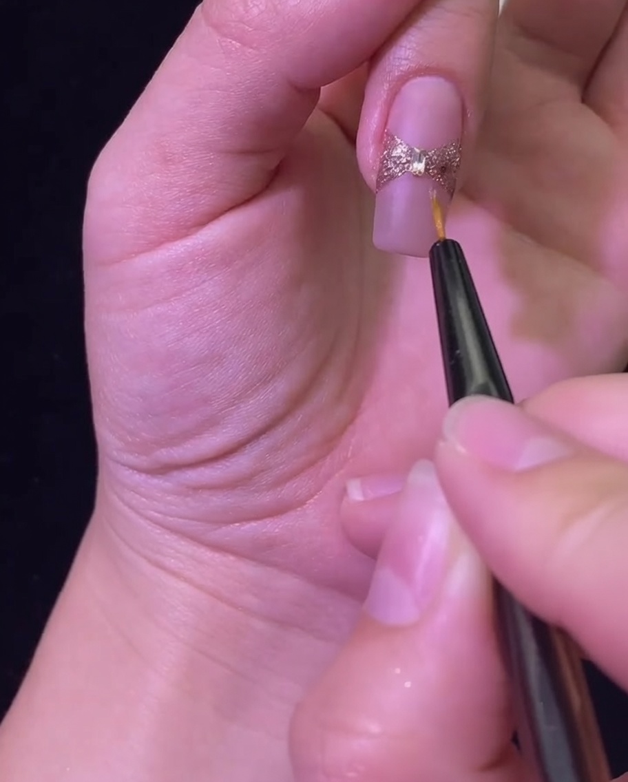 Ein Liner-Pinsel trägt einen glänzenden Top Coat auf, um die Glitzerschleife und den Strassstein zu versiegeln.