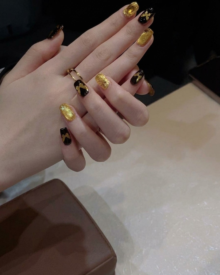 Ein Gelpinsel trägt eine Schicht schimmerndes, goldenes Cat-Eye-Gel auf einen schwarz lackierten Nagel auf.