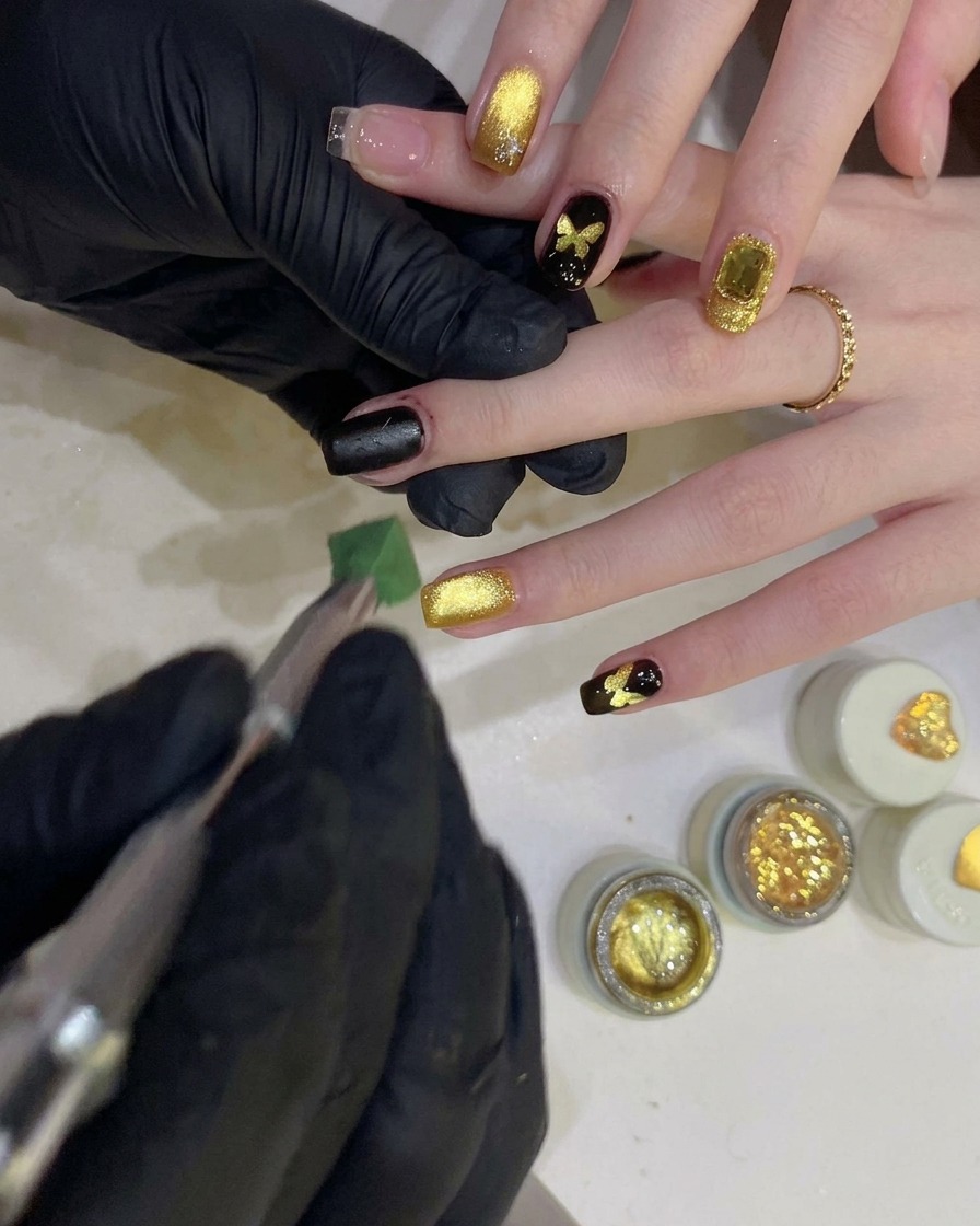 Eine Person tupft mit einem Schwämmchen schwarzes Gel über eine schmetterlingsförmige Schablone auf einem Fingernagel.