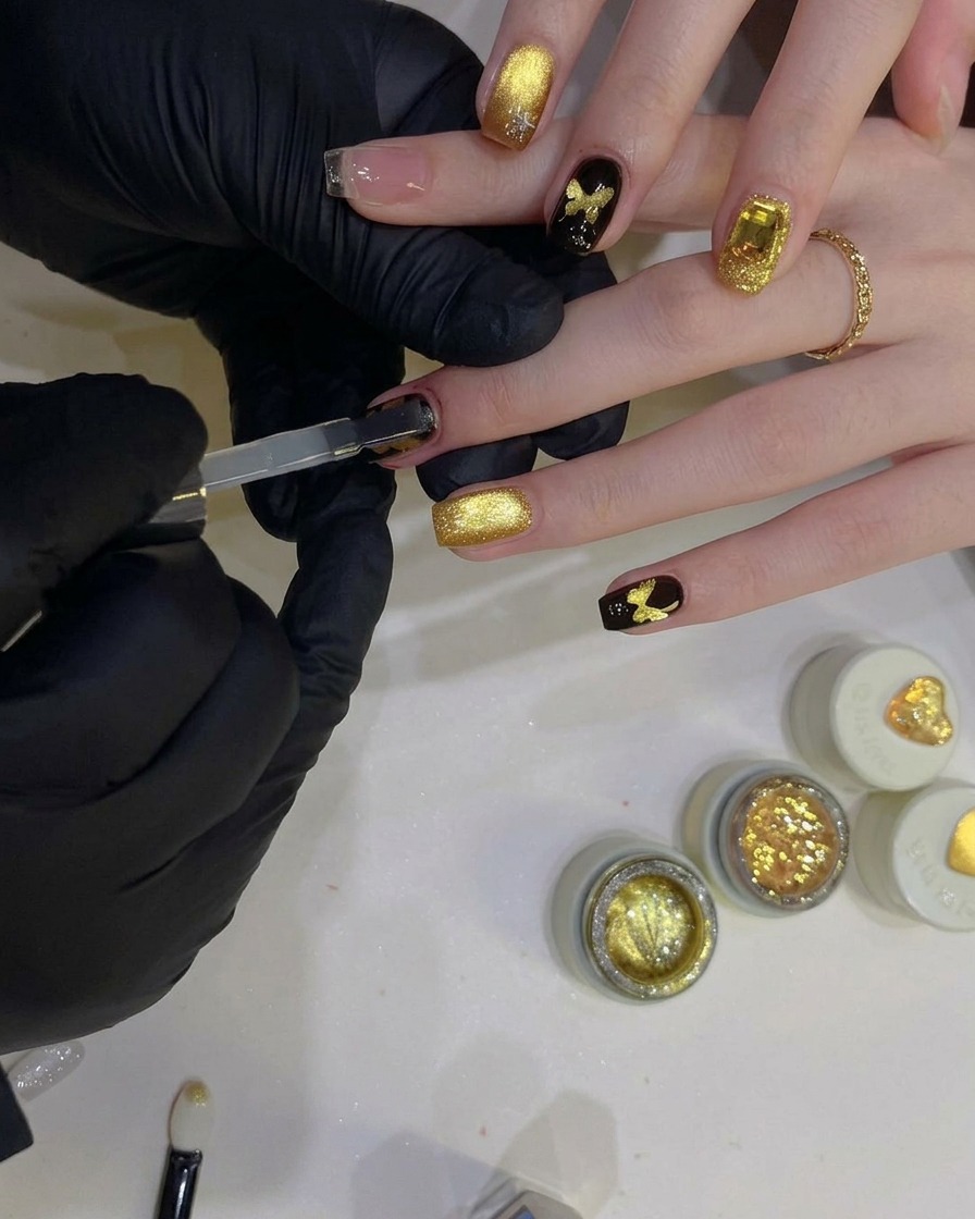 Ein flacher Gelpinsel trägt einen klaren, glänzenden Top Coat über einen schwarzen Nagel mit einem funkelnden goldenen Schmetterlingsdesign auf.