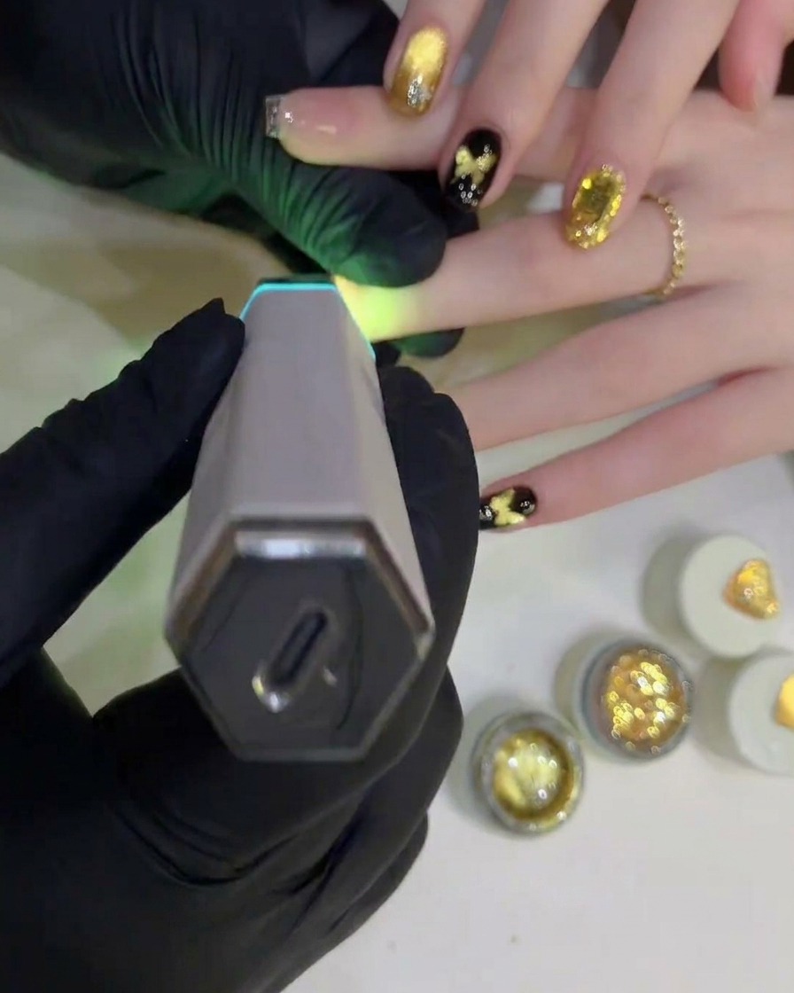Eine Hand-UV-/LED-Lampe wird über einem fertigen Nageldesign positioniert, um den finalen, klaren Top Coat auszuhärten.
