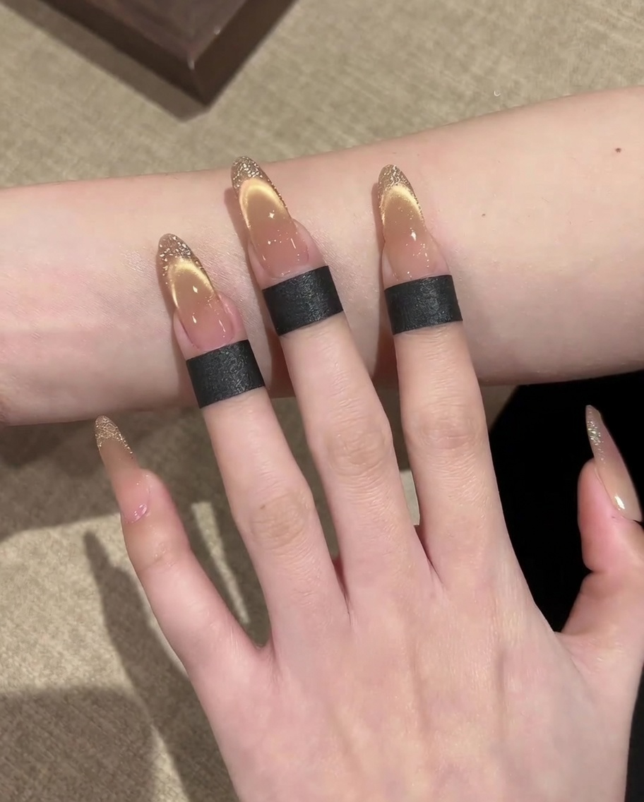 Nahaufnahme einer Hand, die mit einem dünnen Liner-Pinsel eine Goldglitter-Umrandung entlang des Randes eines French-Style Cat-Eye-Nagels malt.
