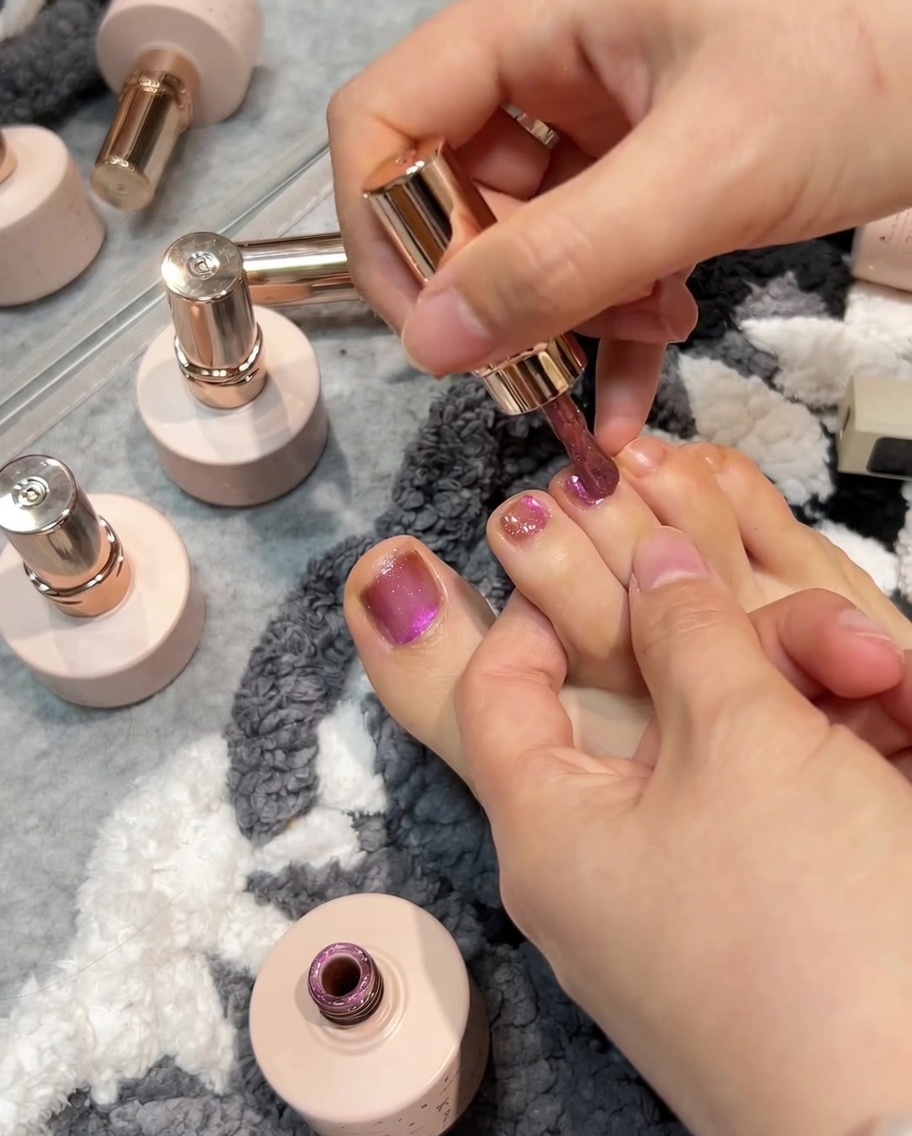 Ein Pinsel trägt rosé-pinken Gellack auf einen Zehennagel auf, gefolgt von der Verwendung eines Magneten zur Erzeugung eines Cat-Eye-Effekts auf der nassen Oberfläche.