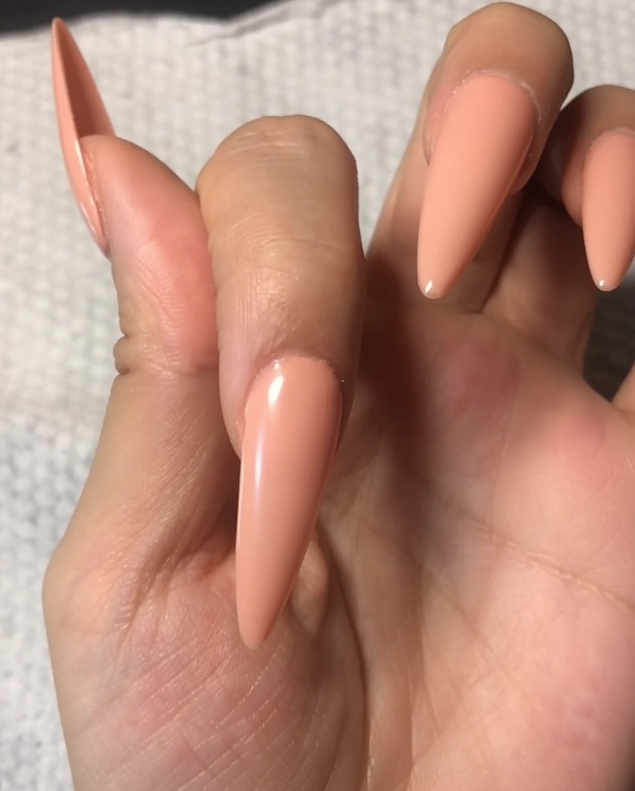 Ein Pinsel trägt einen klaren, glänzenden Top Coat auf einen Fingernagel mit weicher Nude-Basis auf.