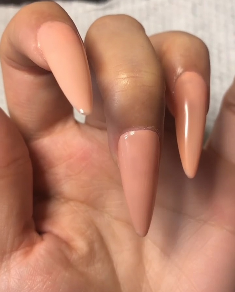 Ein Nagelpinsel trägt eine dünne Schicht Top Coat auf das Nude-Gel des Zeigefingers auf.