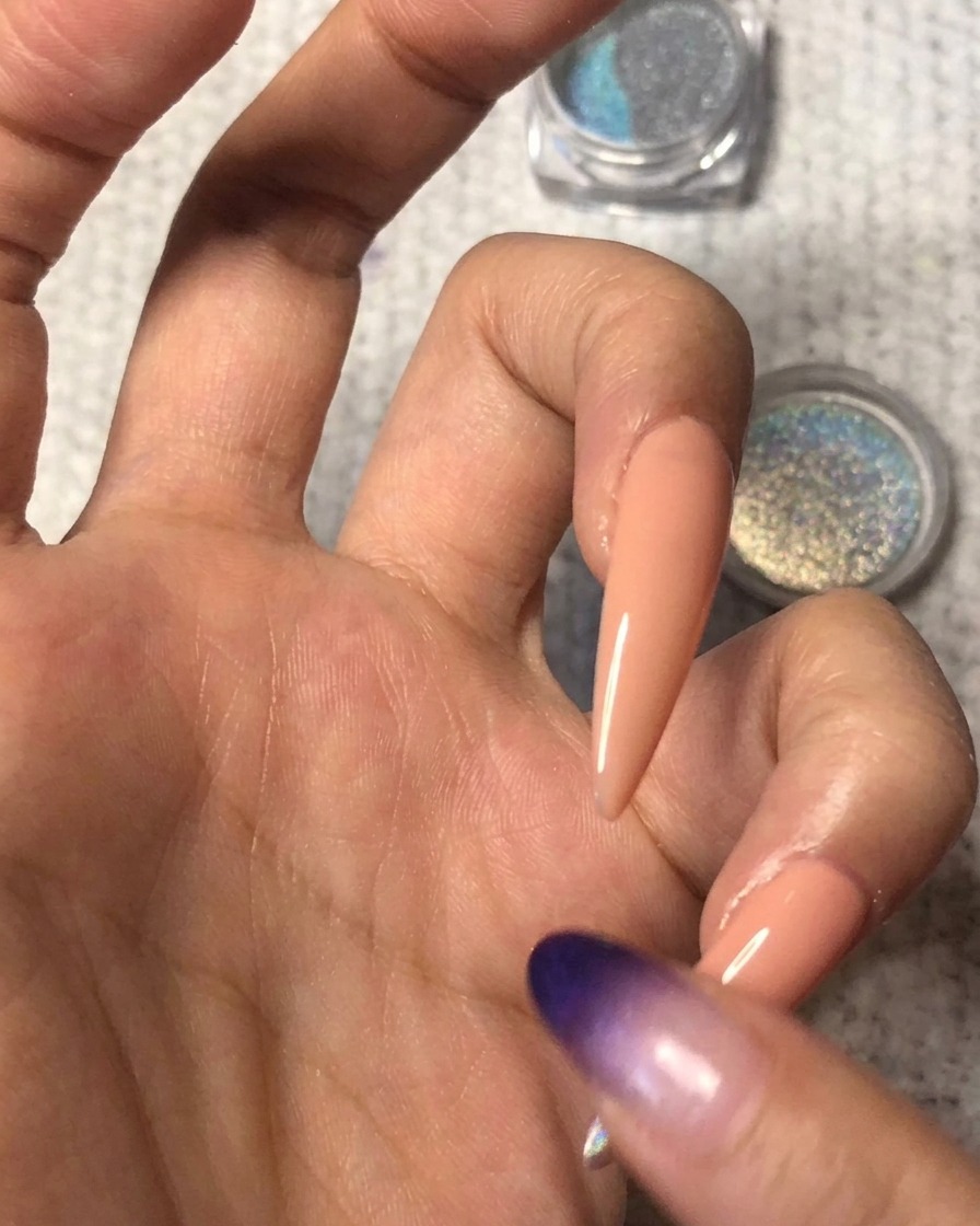Ein sauberer Finger verblendet sanft den Rand des holografischen Puders aufwärts über den Nude-Nagel für einen nahtlosen Ombré-Verlauf.