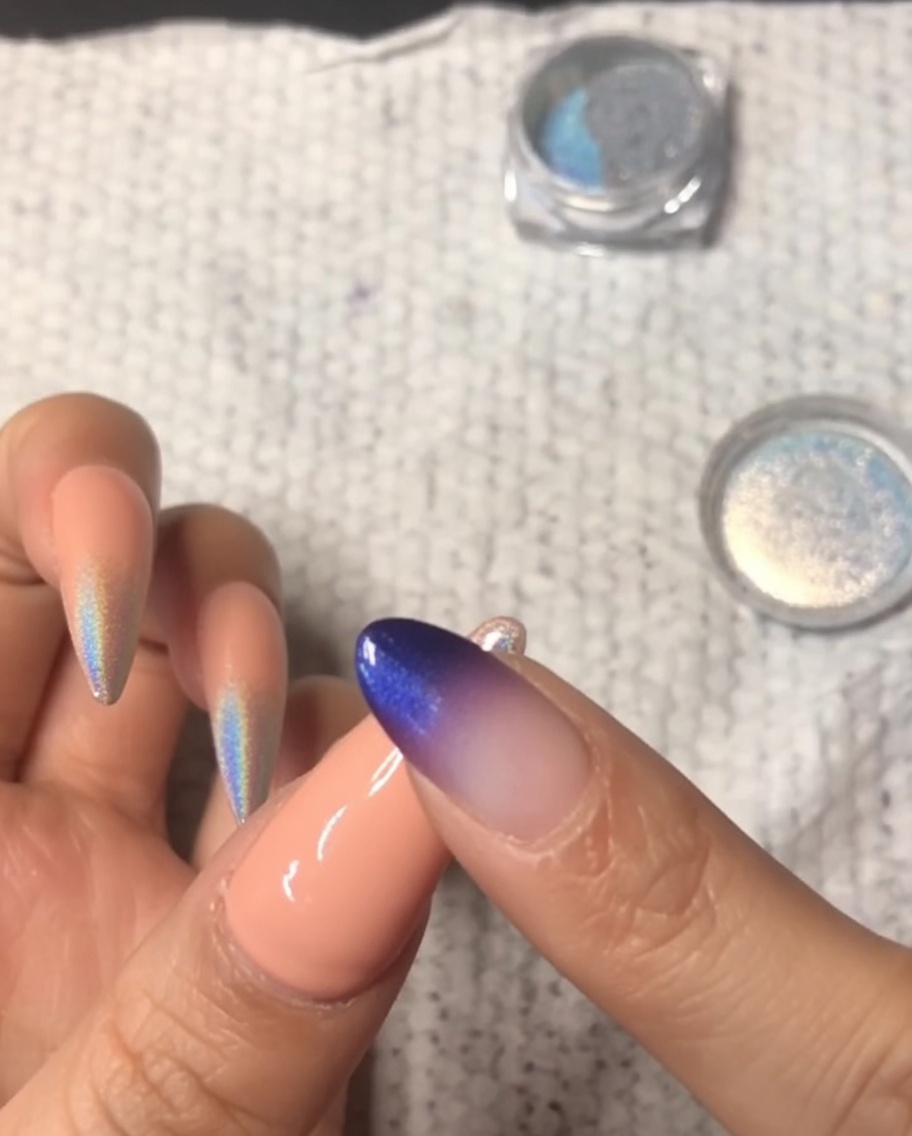 Nahaufnahme eines Fingers, der holografisches Chrom-Puder auf die Spitze eines kleinen Nagels reibt, um einen Ombré-Verlauf zu erzeugen.