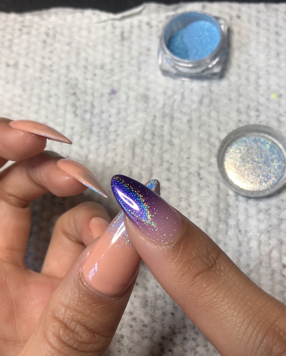 Nahaufnahme eines Fingers, der sanft holografisches Chrom-Puder über die Mitte eines Daumennagels verblendet, um einen weichen Ombré-Fade zu erzeugen.