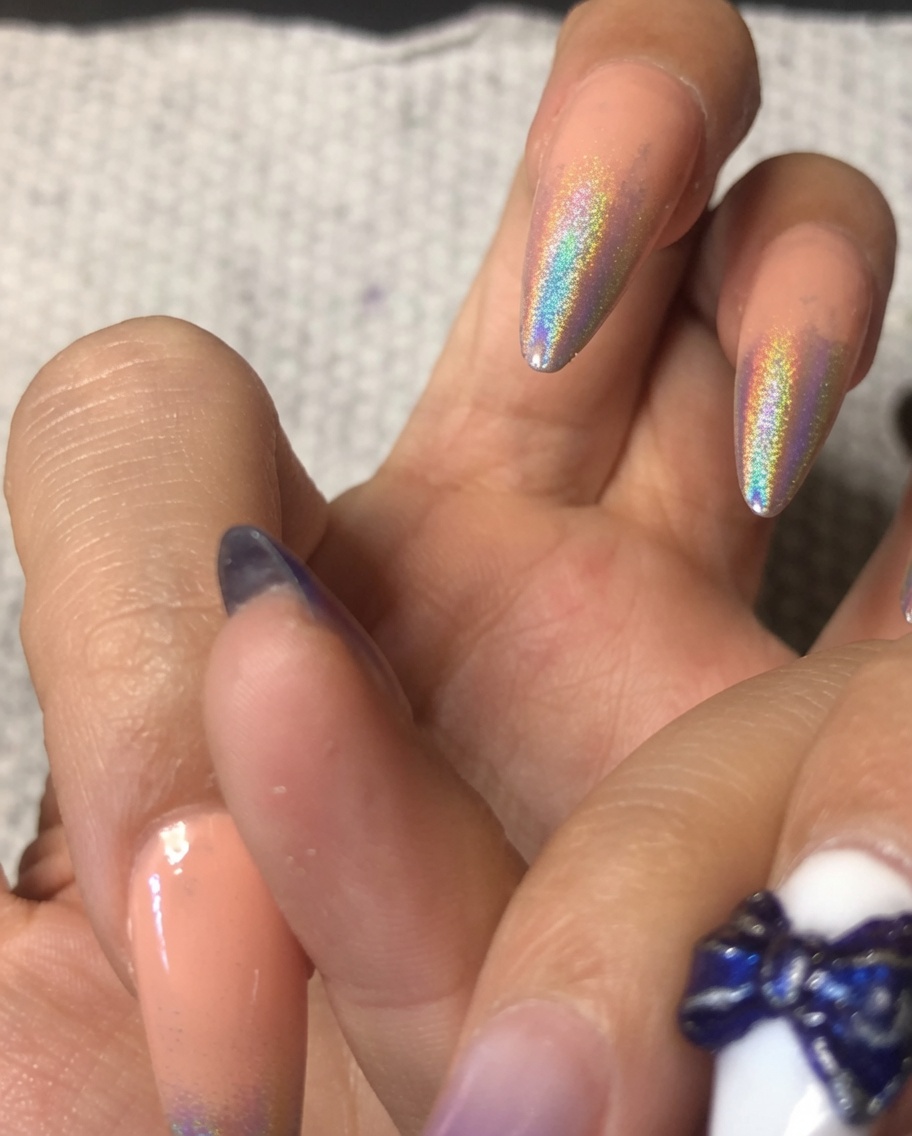 Nahaufnahme eines Pinsels, der eine Schicht klares Gel über einen Zeigefinger mit holografischem Chrom-Ombré-Verlauf aufträgt.
