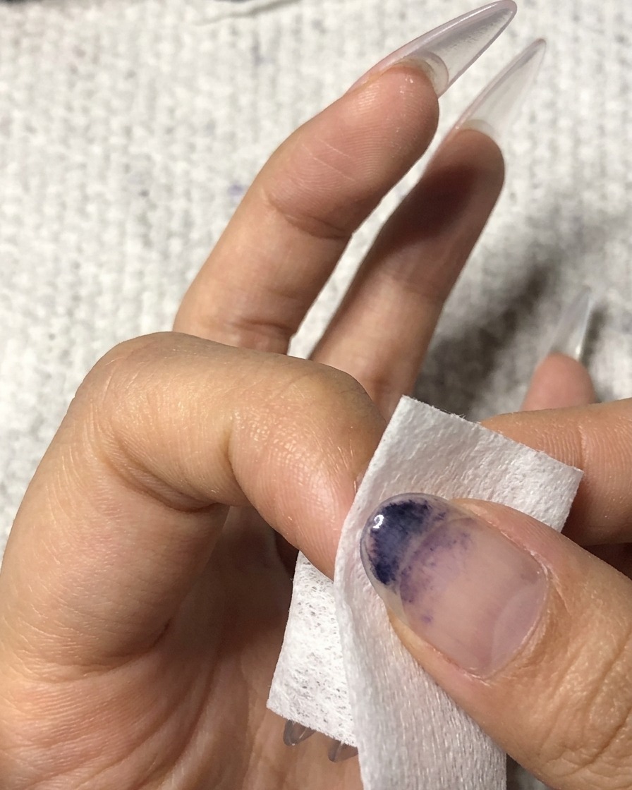 Ein fusselfreies Tuch wird verwendet, um die Oberfläche eines manikürten Ringfingers zu reinigen.