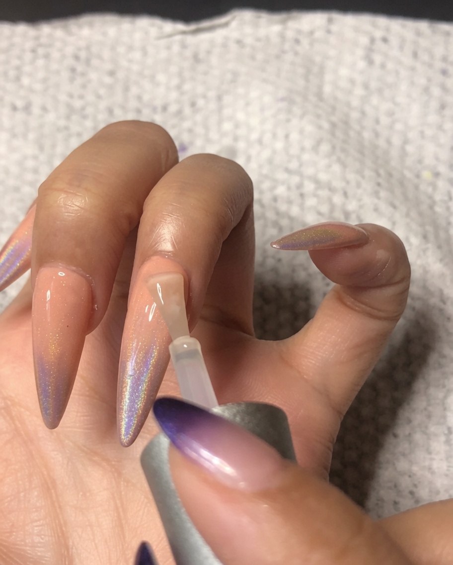 Ein Nagelpinsel trägt einen hochglänzenden Top Coat auf den Ringfinger auf und versiegelt die holografische Ombré-Nail-Art.
