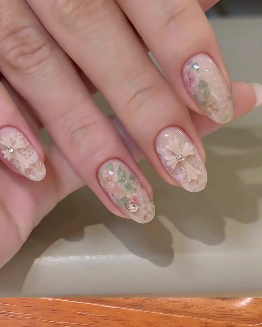 Ein Stück Blumen-Transferfolie wird mit einem Finger auf die Nageloberfläche gedrückt.