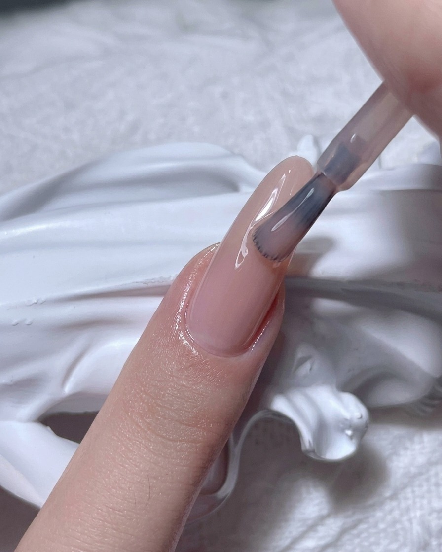 Ein Pinsel trägt ein transparentes Nude-Gel auf einen natürlichen Fingernagel auf.