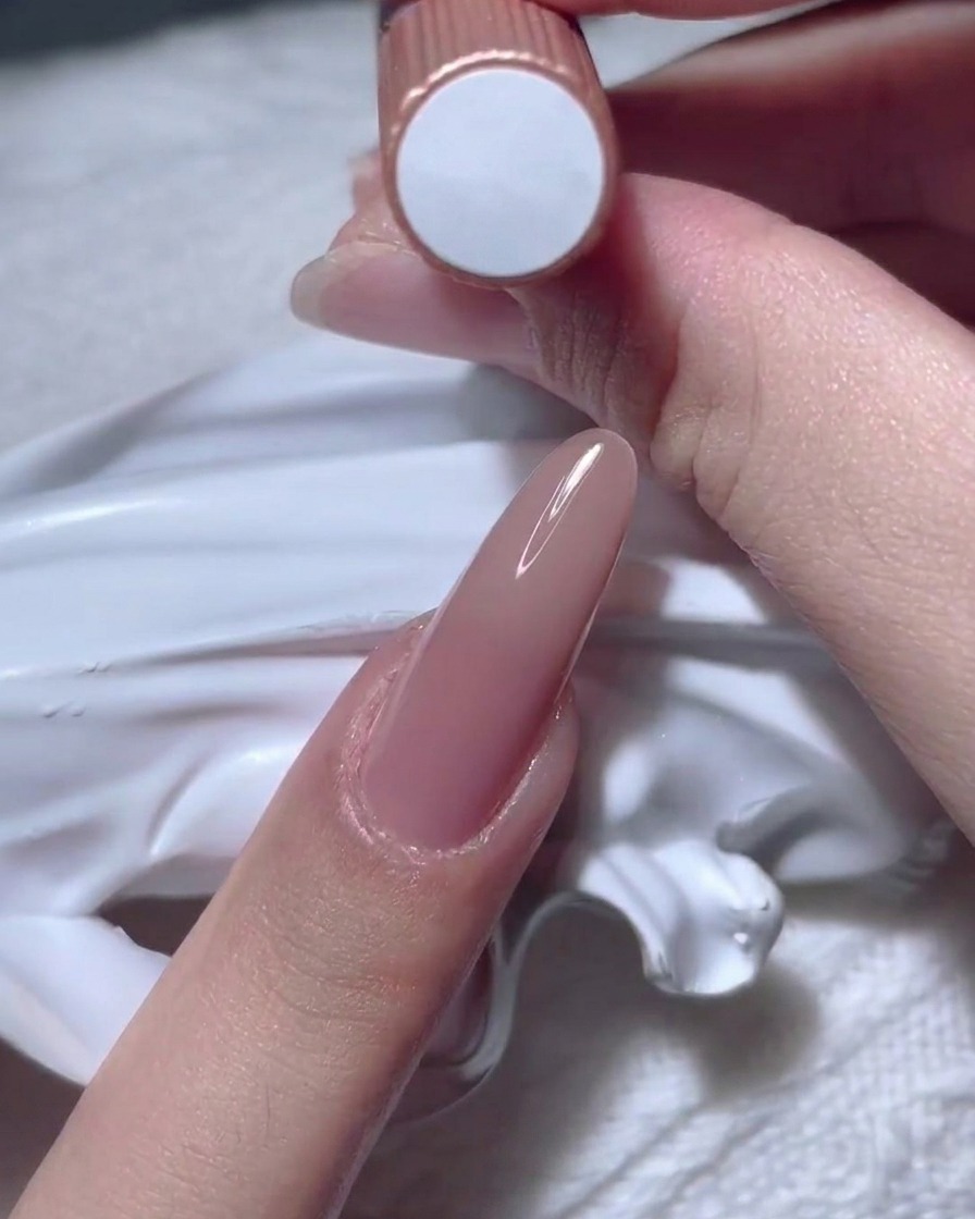 Eine Hand hält eine Flasche mit Nude-Gel-Nagellack hoch.
