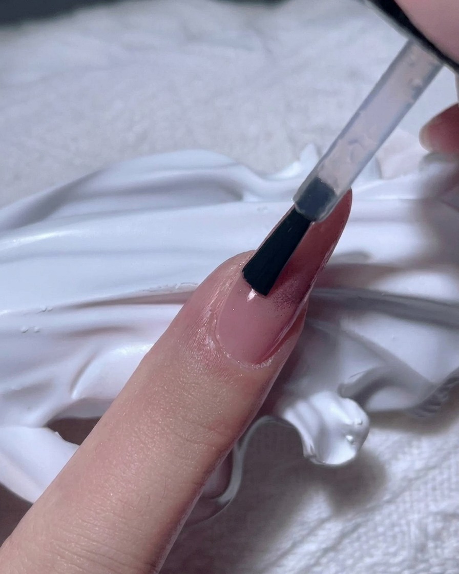 Ein Pinsel trägt ein dickes, klares Gel über einen Roségold-Chrome-Nagel auf.