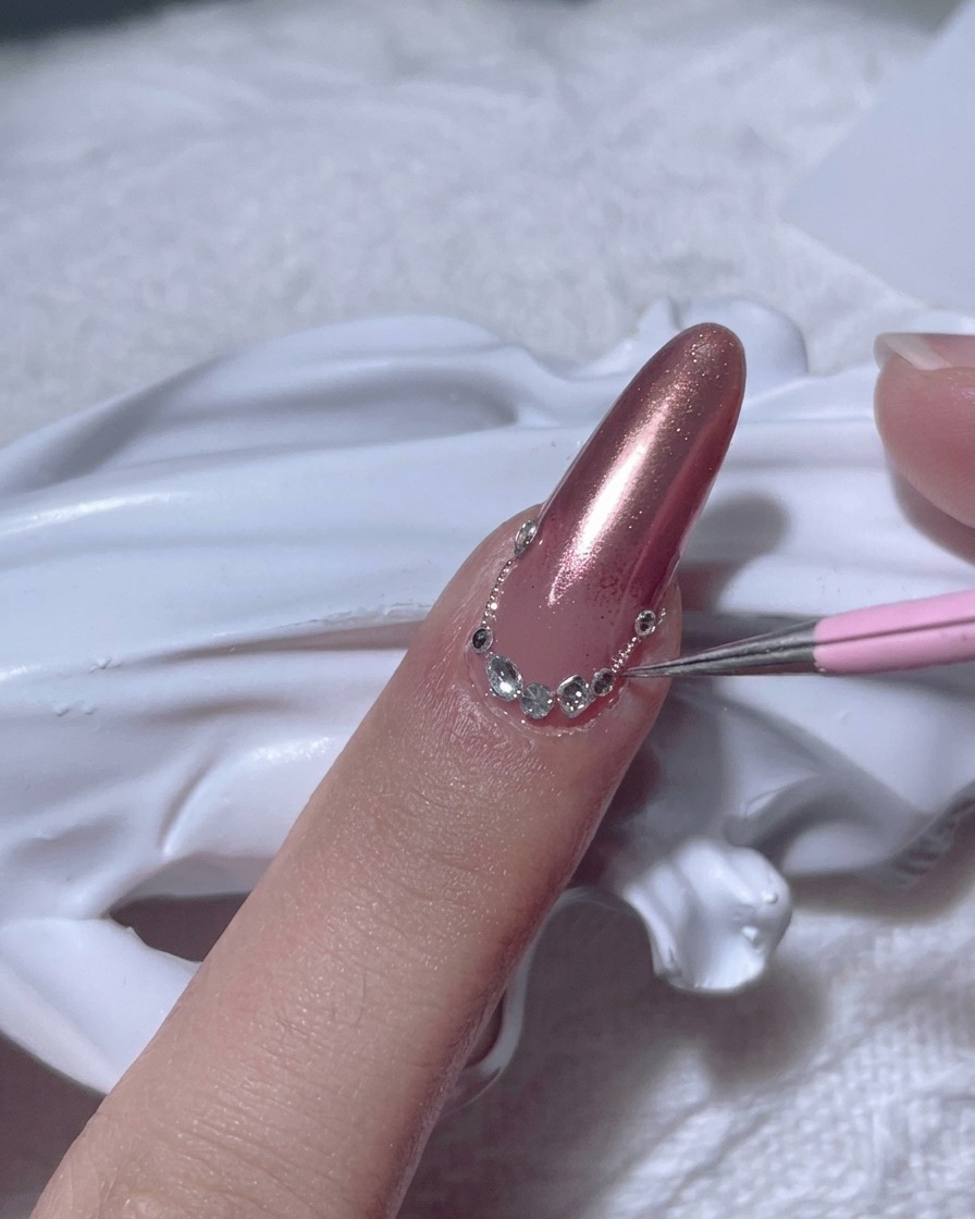 Ein Detail-Tool platziert einen klaren Strassstein nahe der Nagelhaut auf dem Nagel.
