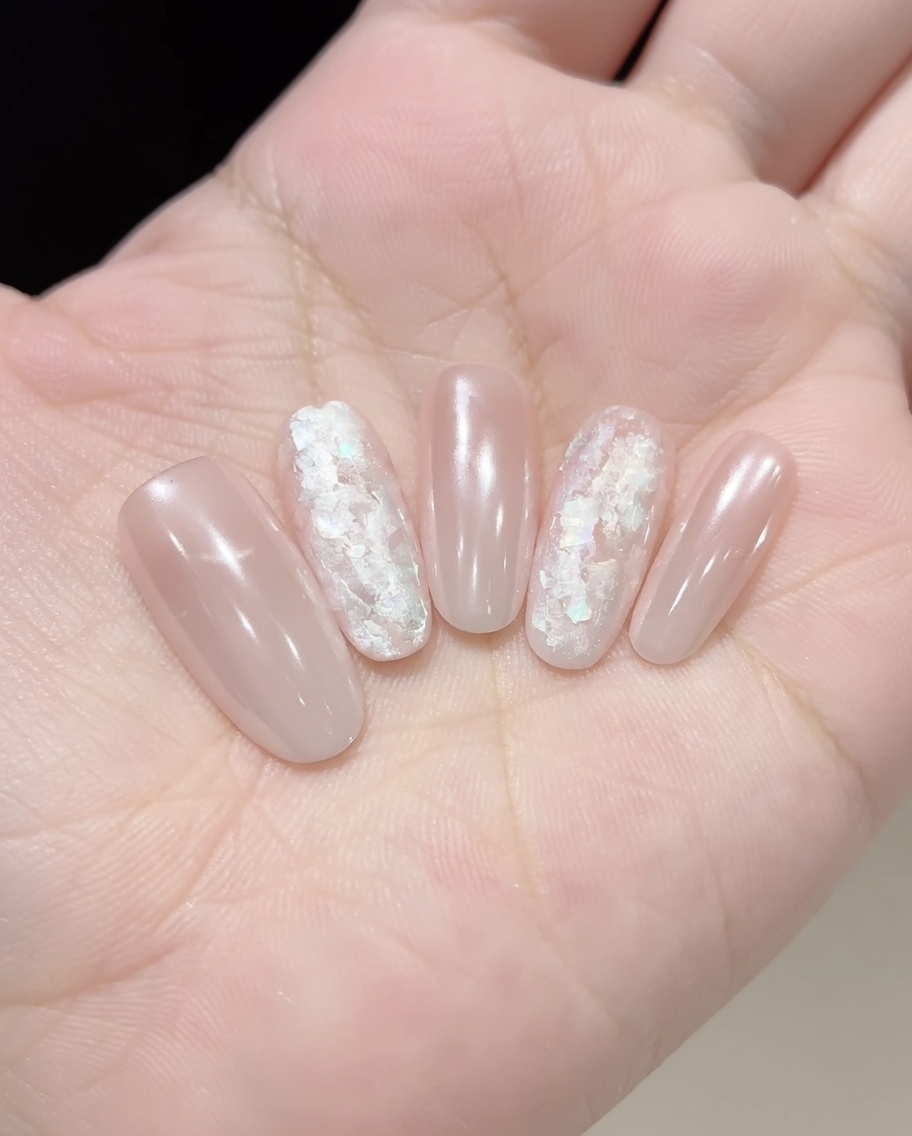 Eine Pinzette oder ein Pinsel platziert irisierende Muschelsplitter auf dem mit Gel überzogenen Nagel.