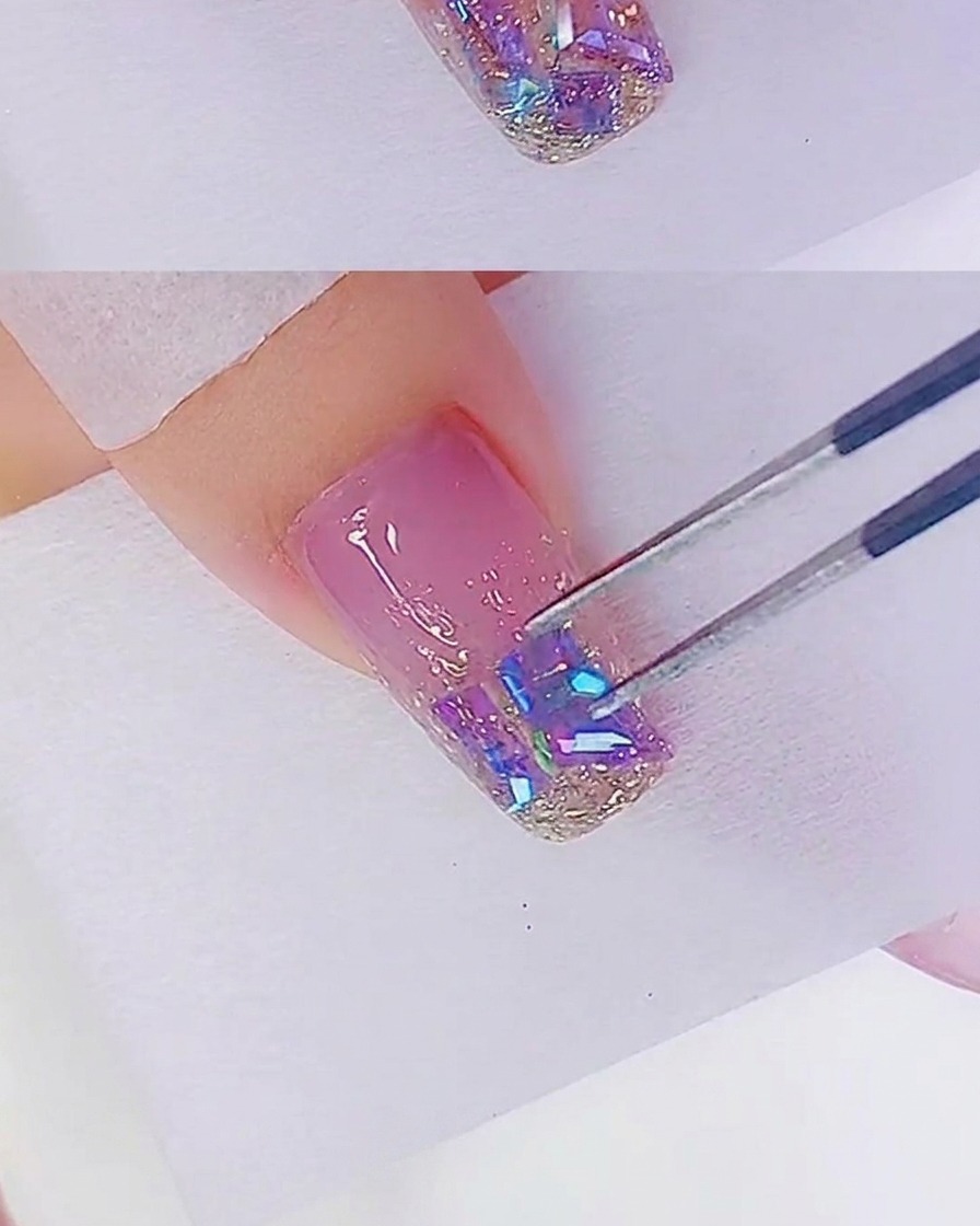 Eine Nahaufnahme zeigt, wie eine Pinzette irisierende Steine auf einer glitzernden Nagelspitze positioniert.