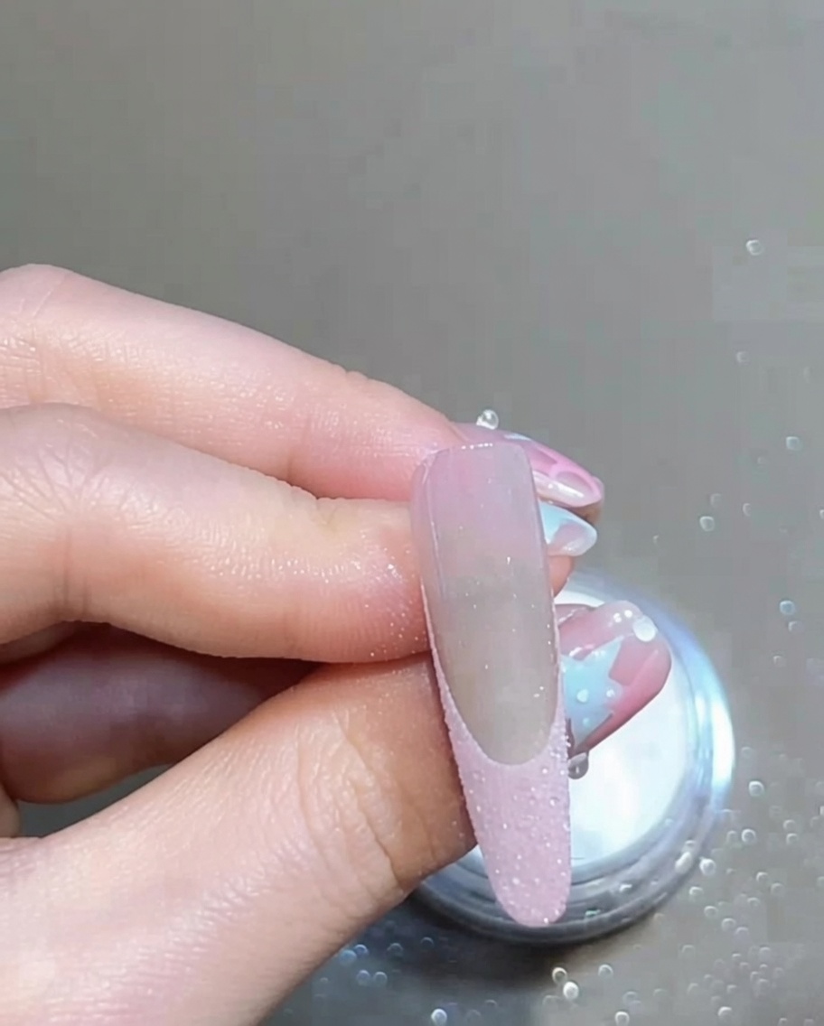 Ein weicher Pinsel wischt über einen manikürten Nagel, um loses Glitzerpuder zu entfernen und eine saubere French-Spitze zu zeigen.