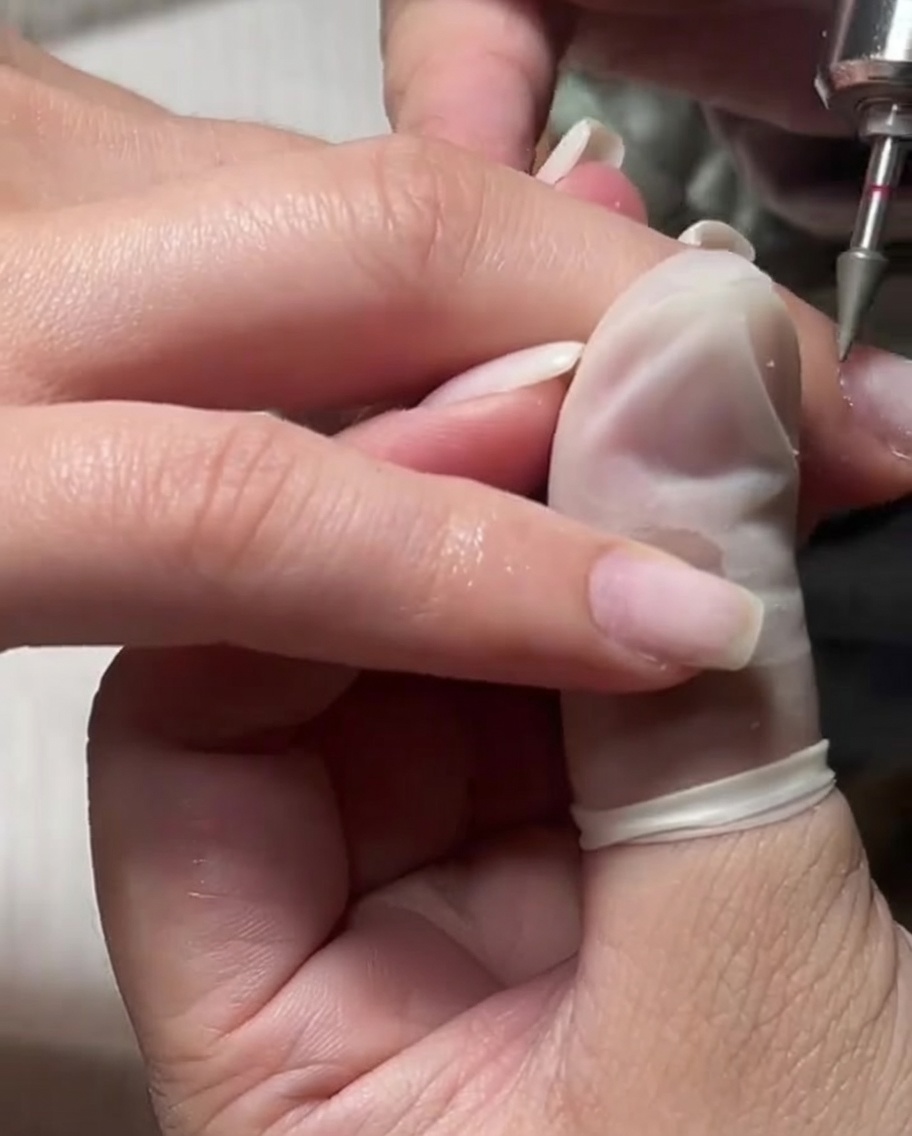 Ein feiner Fräseraufsatz wird an einer befeuchteten Nagelhaut für ein sanftes Peeling verwendet.