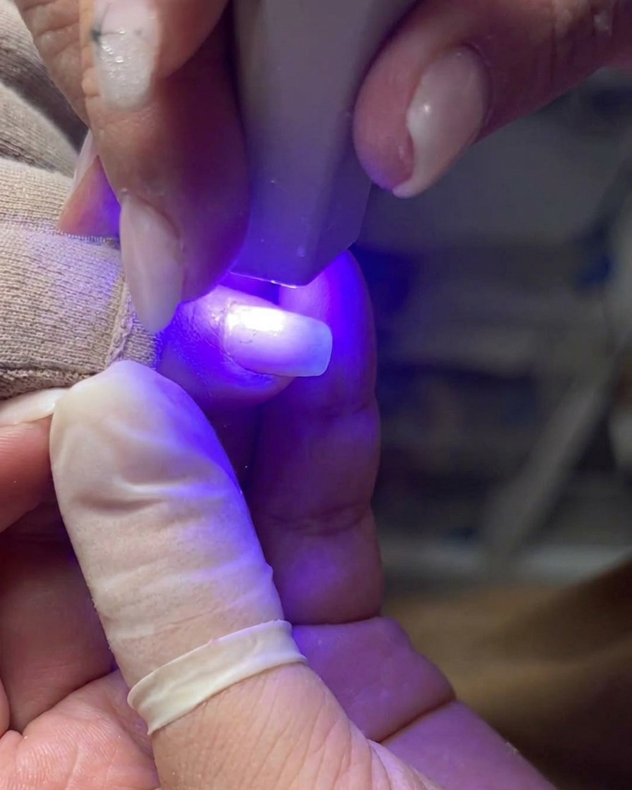 Ein professioneller Nagelpinsel trägt eine gleichmäßige Schicht klares Gel auf eine Naturnagelplatte auf.