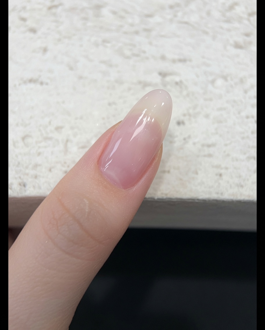 Ein Pinsel trägt einen transparenten, nude-pinken Jelly-Gellack auf einen Naturnagel auf.