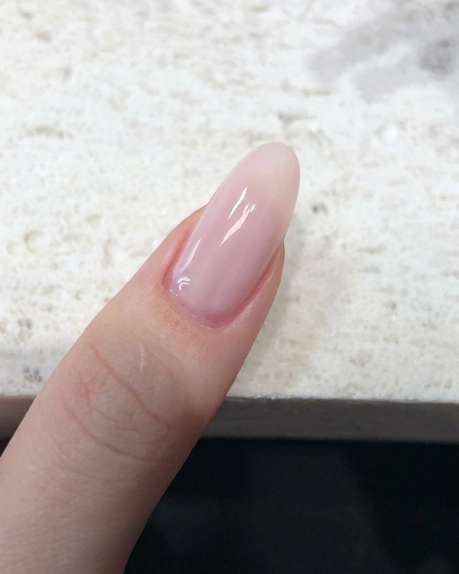 Nahaufnahme eines Fingernagels, der mit einem transparenten, nude-pinken Jelly-Lack beschichtet ist und ein glattes Finish aufweist.