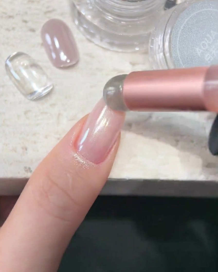 Ein Schwammapplikator trägt Aqua-Chrom-Puder auf eine glatte, glänzende Nageloberfläche auf.
