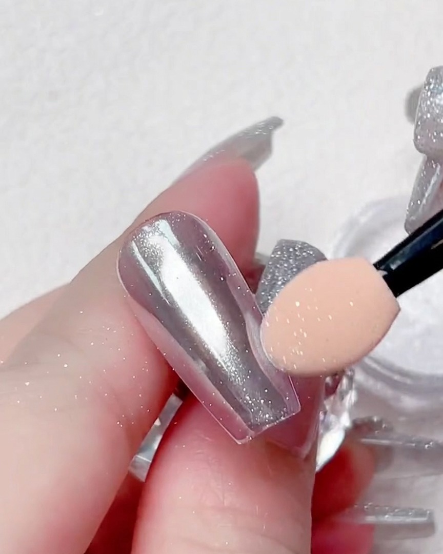 Nahansicht, wie der Applikator Chrom-Puder auf die Ränder eines transparenten Nageltips poliert.