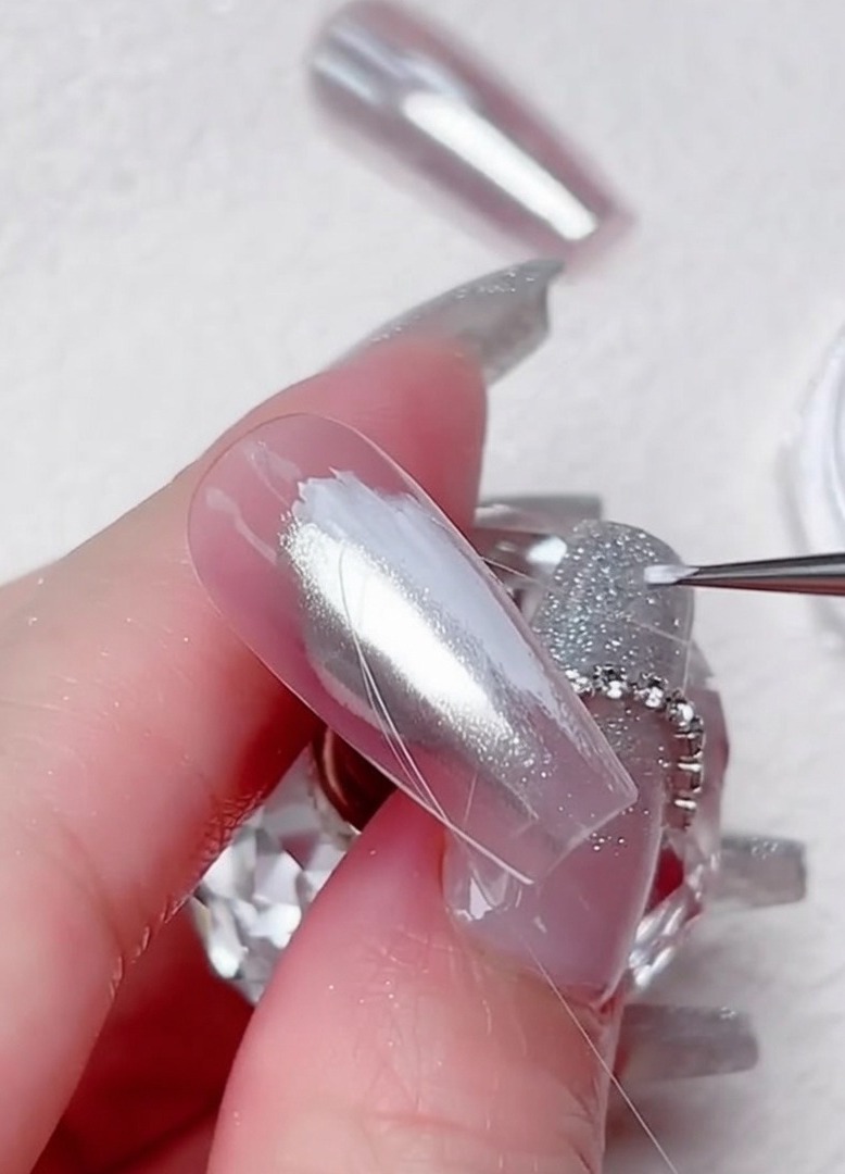 Ein feiner Liner-Pinsel zieht dünne, klare Gel-Linien in einem diagonalen Muster über einen silbernen Chromnagel.