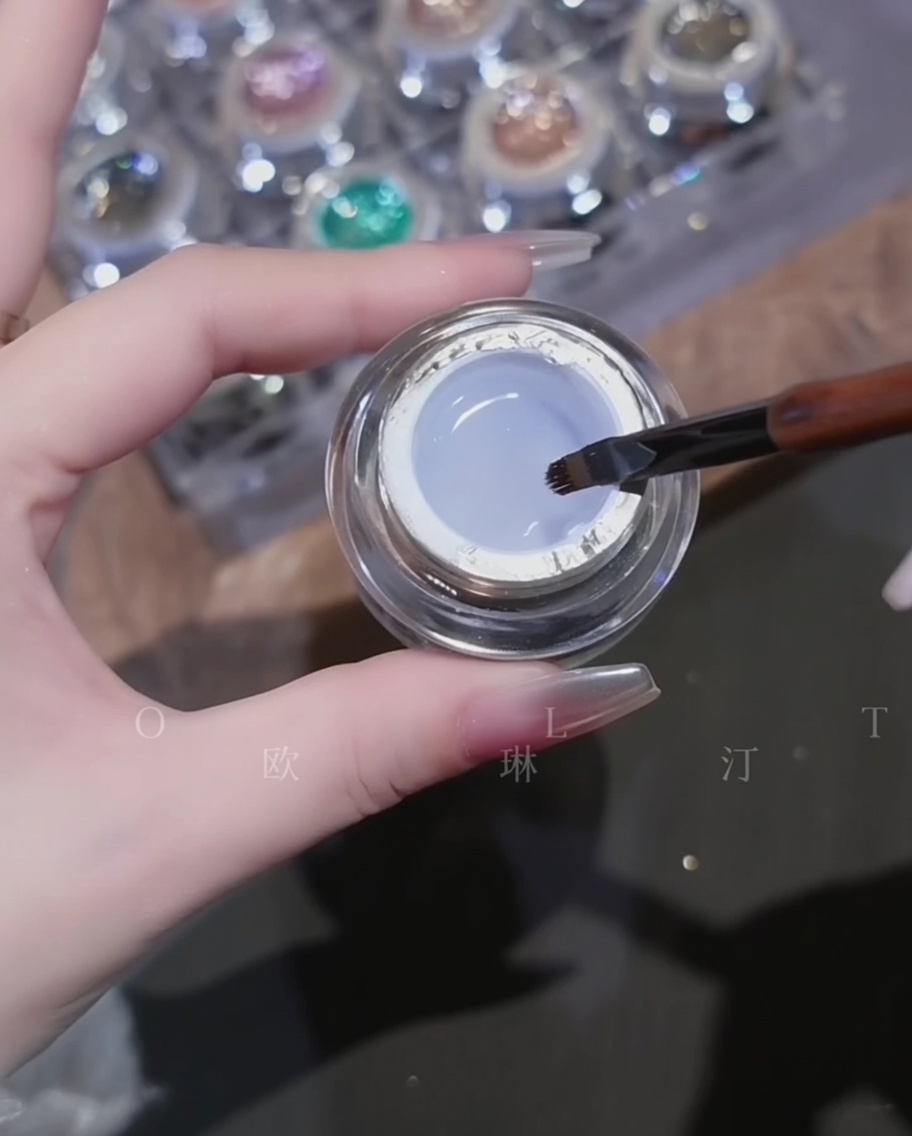 Ein Pinsel trägt klares, zähflüssiges Aufbaugel über einen Chrome-Nagel auf.