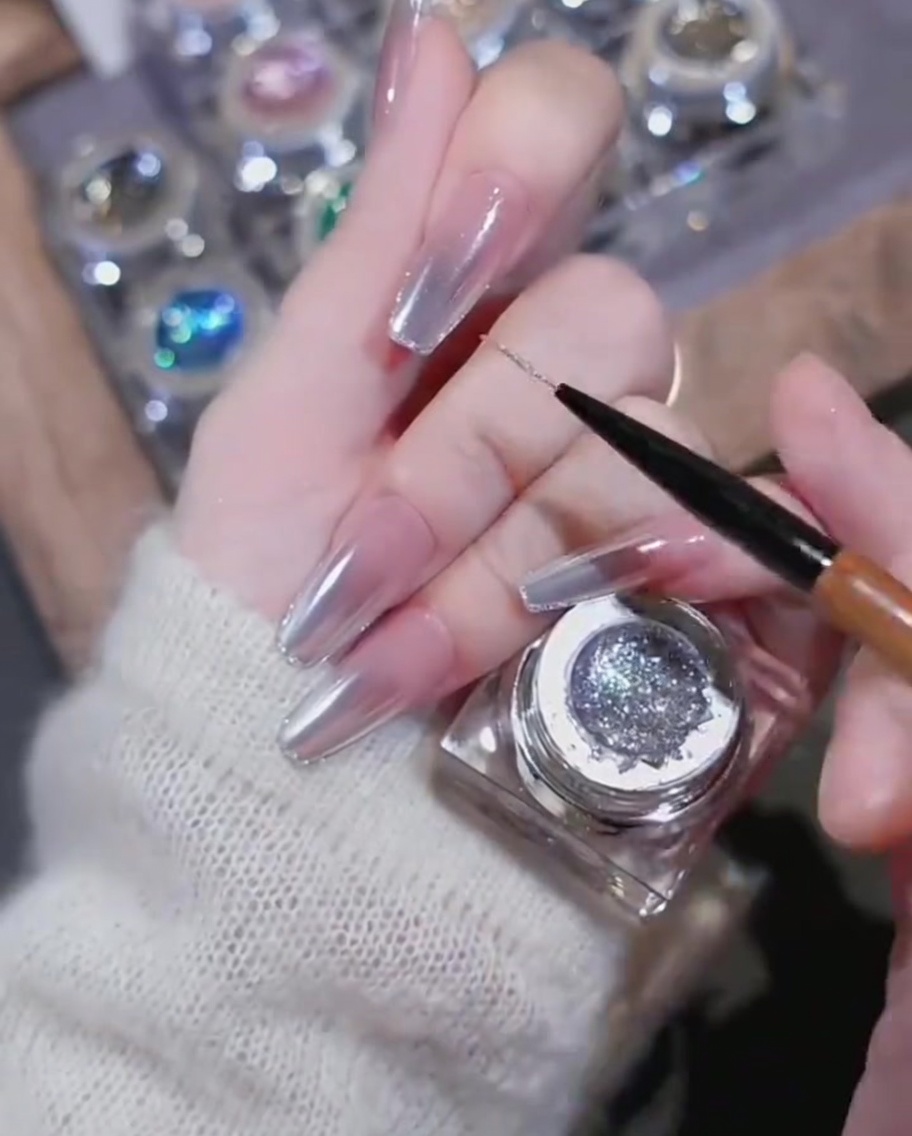 Ein herzförmiger Strass-Charm wird auf einen Nagel mit Glitzerlinien gesetzt.