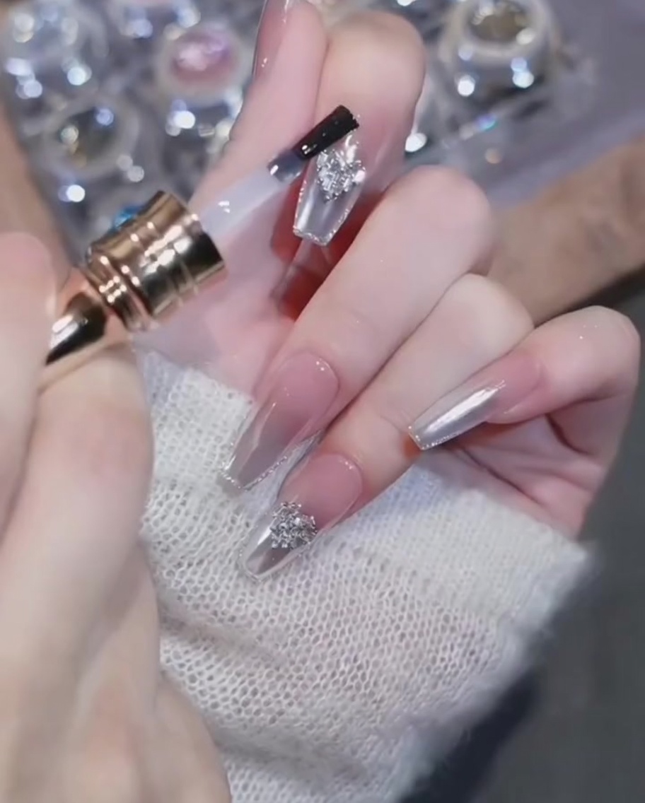 Ein Top-Coat-Pinsel umrandet vorsichtig einen Herz-Charm auf einem Chrome-Nagel.