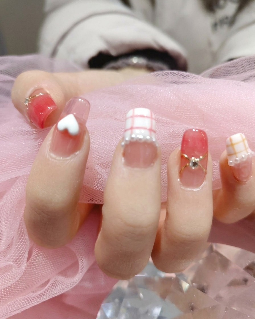 Ein Werkzeug platziert winzige, schimmernde weiße Perlen um die Basis der Nagelkunst-Designs auf einer manikürten Hand.