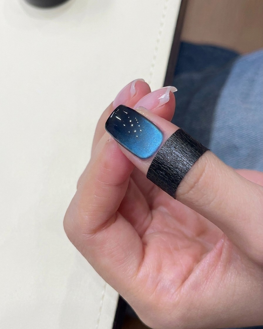 Ein Pinsel trägt schwarzes Gel auf die Nagelspitze auf.