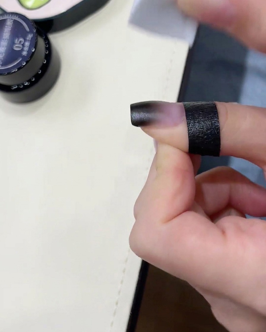 Ein Schwamm verblendet schwarzes Gel auf einem Nagel.