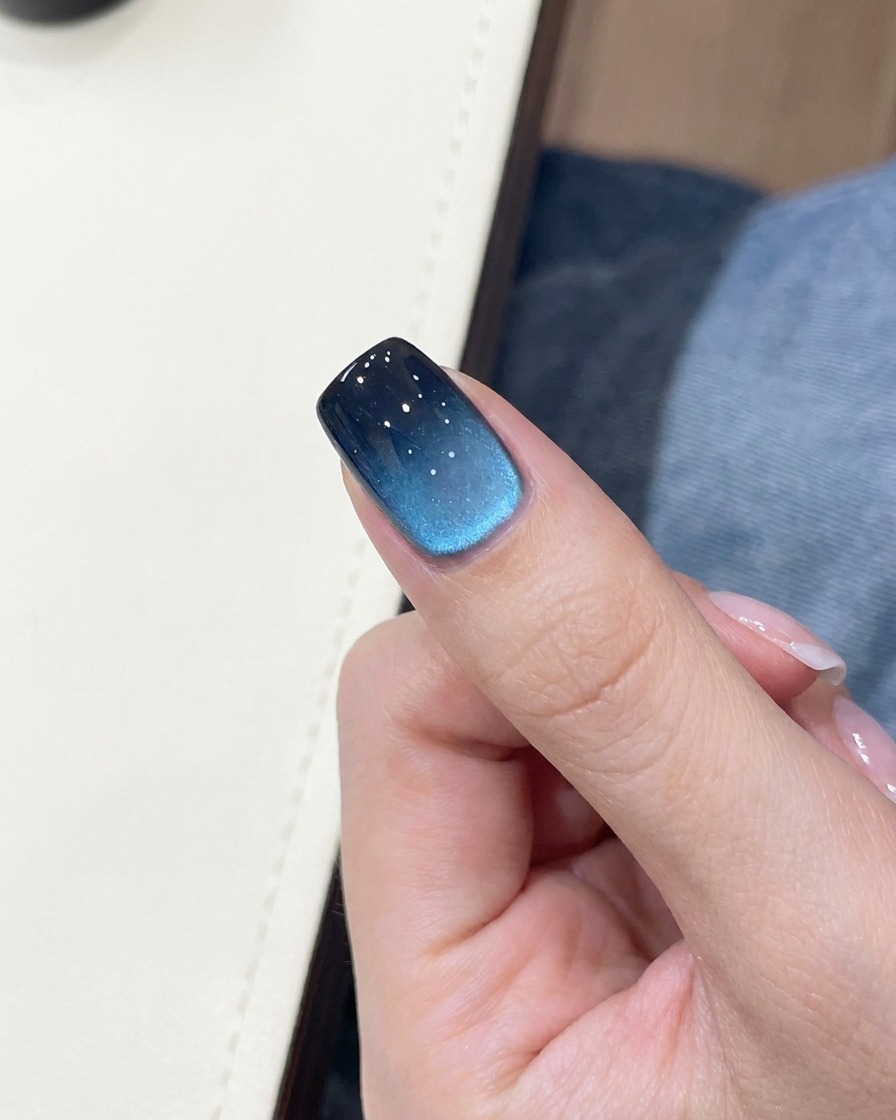 Nahaufnahme eines blau-schwarzen Verlauf-Nagels mit kleinem, goldenem Schmetterlings-Sticker.