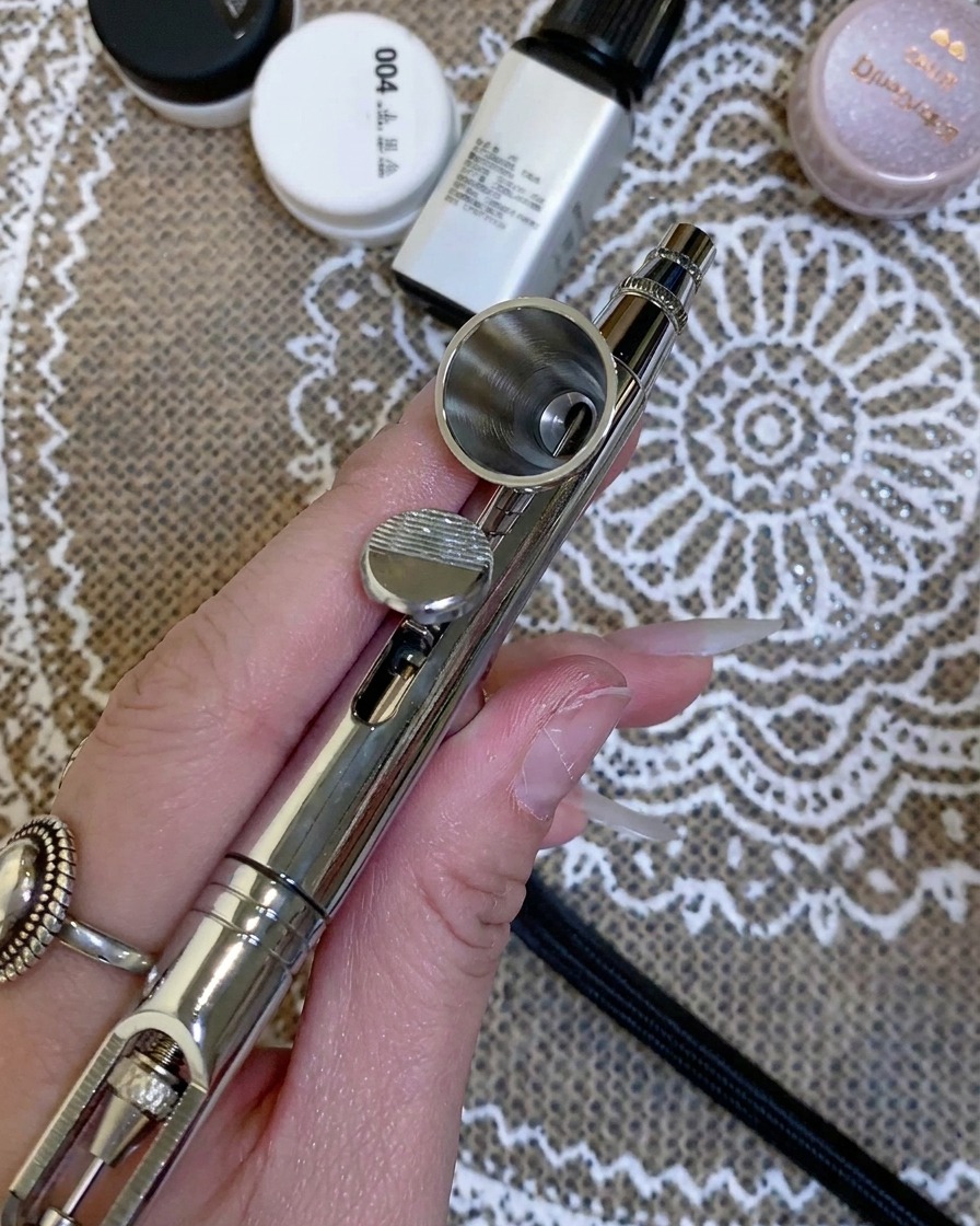 Hand hält eine Airbrush-Pistole, während klare Flüssigkeit in den Metallbehälter gegeben wird.